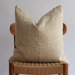 May include: A beige linen pillow sits on a wooden chair with a woven seat.