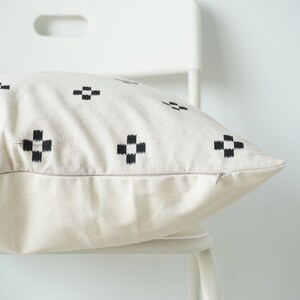 May include: A white pillow with a black geometric pattern. The pillow is sitting on a white chair.