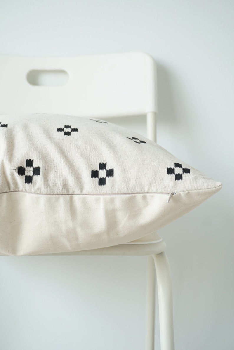 May include: A white pillow with a black geometric pattern. The pillow is sitting on a white chair.