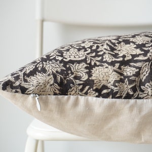 Puede incluir: Una almohada con estampado floral en blanco y negro con cierre de cremallera. La almohada est&aacute; sentada en una silla blanca.
