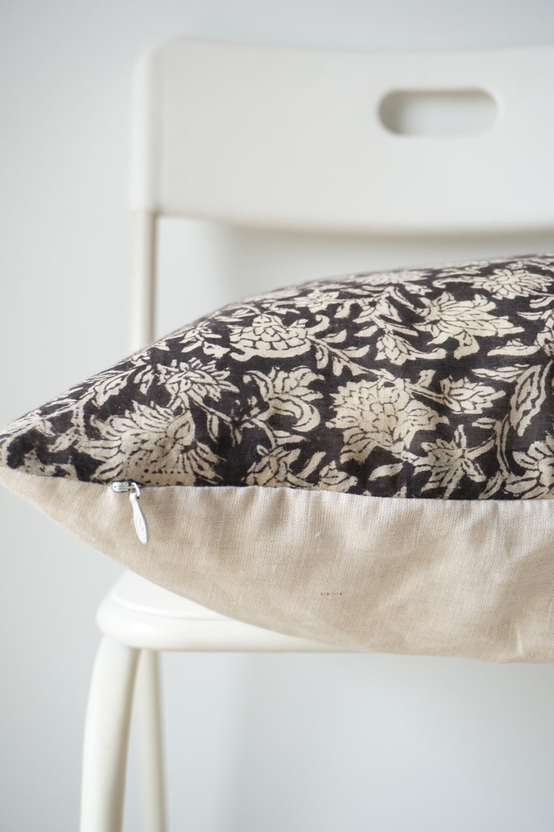 Puede incluir: Una almohada con estampado floral en blanco y negro con cierre de cremallera. La almohada est&aacute; sentada en una silla blanca.