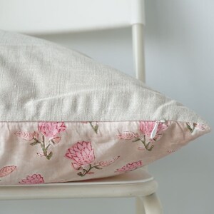 May include: A light pink pillow with a floral print of pink flowers on a white linen background. The pillow has a zipper closure.