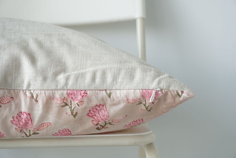 May include: A light pink pillow with a floral print of pink flowers on a white linen background. The pillow has a zipper closure.