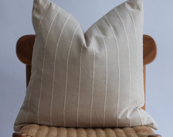 May include: A beige striped pillow with white stitching sits on a woven chair with wooden legs.