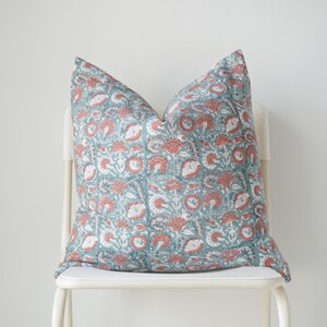 Puede incluir: Una almohada con estampado floral de color azul verdoso y coral sobre una silla blanca.