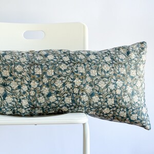 May include: A teal blue and white floral patterned lumbar pillow resting on a white chair.