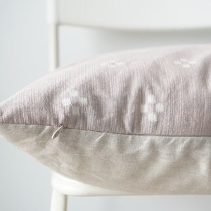 May include: A close-up of a light pink throw pillow with a white geometric pattern. The pillow has a hidden zipper closure and a light beige linen backing.