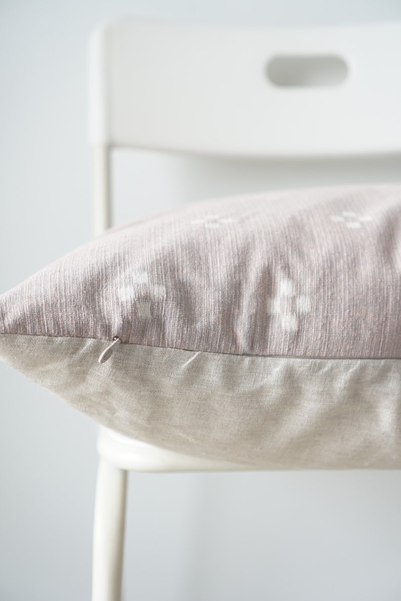 May include: A close-up of a light pink throw pillow with a white geometric pattern. The pillow has a hidden zipper closure and a light beige linen backing.