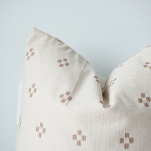 May include: A white pillow with a brown geometric pattern. The pillow is made of a soft, textured fabric.