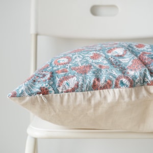 Puede incluir: Una almohada con estampado floral de color azul verdoso y coral con cierre de cremallera y respaldo de lino beige.