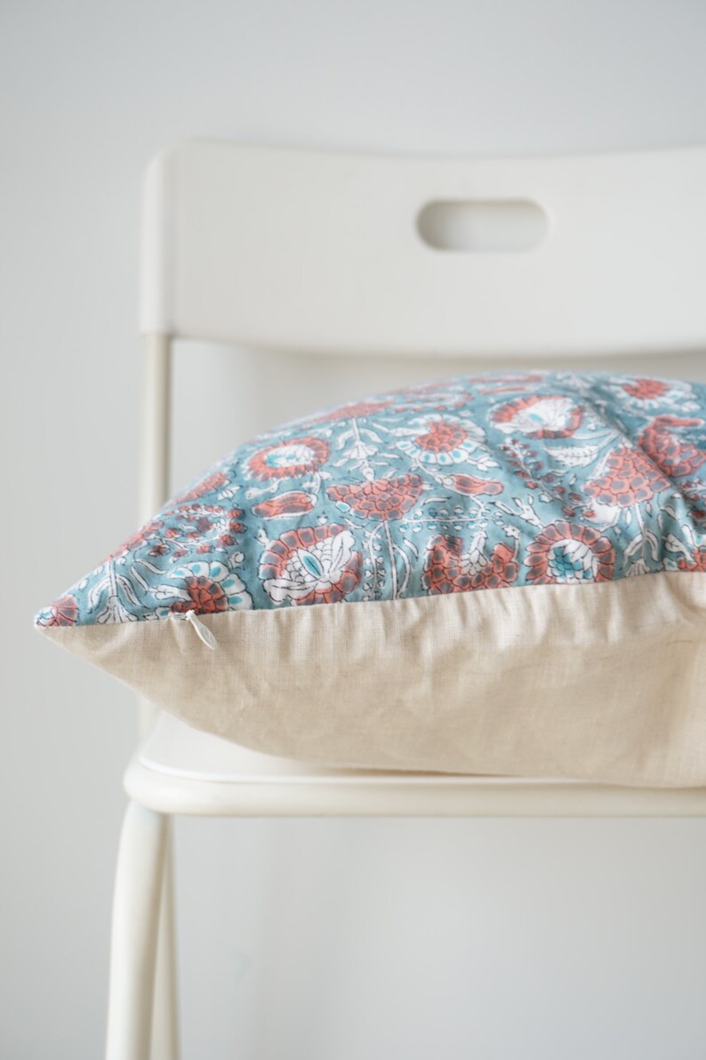 Puede incluir: Una almohada con estampado floral de color azul verdoso y coral con cierre de cremallera y respaldo de lino beige.