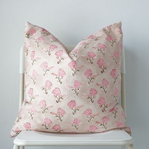 May include: A pink and green floral patterned cushion on a white chair.