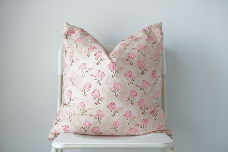 May include: A pink and green floral patterned cushion on a white chair.