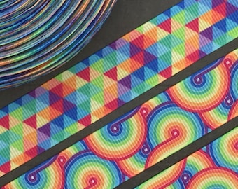 May include: Two colorful ribbon trims with rainbow geometric patterns. The first trim features a repeating pattern of triangles in shades of red, orange, yellow, green, blue, indigo, and violet. The second trim features a repeating pattern of curved lines in shades of red, orange, yellow, green, blue, indigo, and violet.