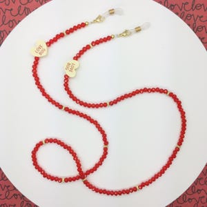 May include: Red beaded eyeglass chain with gold accents and heart-shaped charms. The charms have the words "LOVE BUG" printed on them. The chain has a loop at each end to attach to eyeglasses.