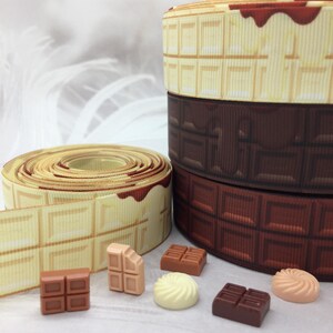 May include: Rolls of white and brown chocolate patterned ribbon with a chocolate drizzle.  There are also several small chocolate candies in the image.