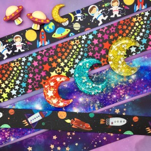May include: Five different space-themed ribbon trims with colorful astronaut, rocket, star, and crescent moon designs. The ribbons are layered on top of each other, creating a colorful and whimsical pattern.