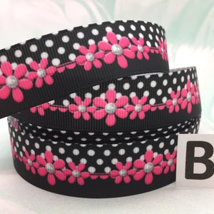 May include: Black and white polka dot ribbon with a row of pink flowers with silver centers. The ribbon is rolled up and the letter "B" is visible on a white label.