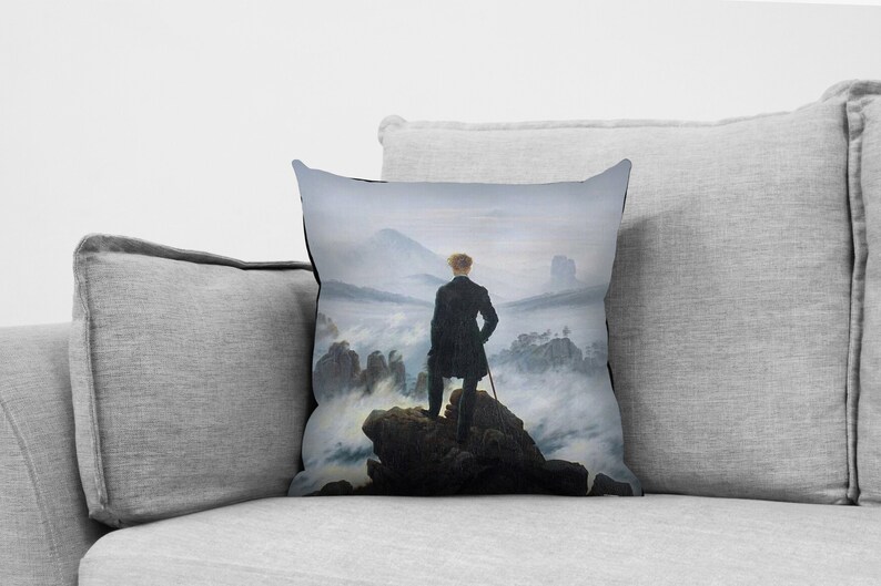 May include: A throw pillow featuring a painting of a man standing on a mountaintop overlooking a sea of clouds. The painting is in a muted color palette of grays, blues, and greens.
