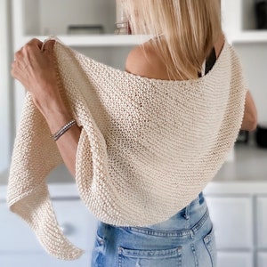 May include: A cream-coloured knitted shawl draped over a person's shoulders. The shawl is made of a soft, lightweight yarn and has a simple, elegant design.