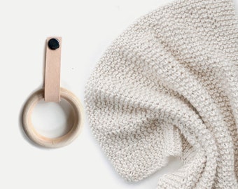 Puede incluir: Una manta de punto blanco con un anillo de madera y una correa de cuero.