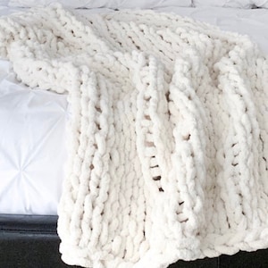 May include: A white chunky knit throw blanket with a soft, fluffy texture.