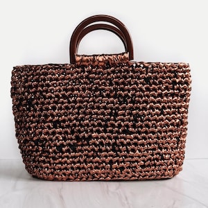 May include: A woven copper-colored tote bag with wooden handles. The bag is made of a tightly woven material and has a slightly textured surface.