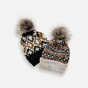 Puede incluir: Dos gorros de invierno de punto con pompones. Los gorros son negros, blancos y marrones con un patrón geométrico.