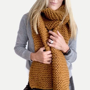 May include: A chunky knit scarf in a warm mustard yellow color. The scarf is made of a soft, textured yarn and is long enough to be worn in a variety of ways.