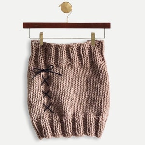 May include: A brown knitted skirt with black ribbon detailing. The skirt is hanging on a wooden hanger.