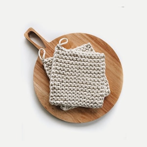 May include: Two beige knitted pot holders on a round wooden cutting board with a handle.