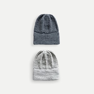 May include: Two knitted beanies, one gray and one dark blue. Both beanies have a cable knit pattern and a folded brim.