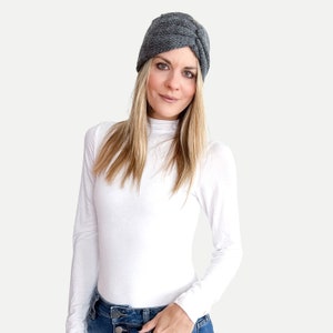 May include: A gray knit turban headband with a twist detail. The headband is worn by a person with long blonde hair, a white turtleneck shirt, and blue jeans.