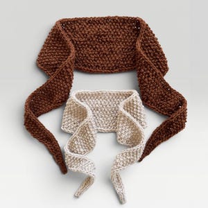 May include: Two knitted headbands featuring a textured garter stitch pattern. One headband is a deep chocolate brown colour, while the smaller, nested headband is a light cream colour. Both items have long, tapered ends that extend outwards.