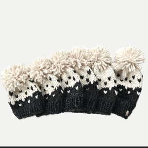 May include: Set of five black and white knit hats with pom poms. The hats have a fair isle pattern with white hearts on a black background.