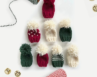 May include: Eight miniature knitted hats with pom-poms in red, white and green. The hats are arranged in a triangular shape on a white background.