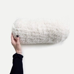 May include: A white fluffy cylindrical pillow. The pillow is soft and appears to be made of a plush material.