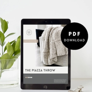 May include: A digital tablet displaying a knitting pattern for a throw blanket called "The Piazza Throw". The pattern is from Lili Knit Designs and includes a difficulty rating. The text "PDF Download" is displayed in a black circle on the screen.