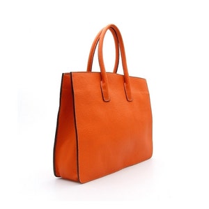 May include: A bright orange handbag with a textured surface, featuring two vertical handles attached to the top panel. The bag has a structured rectangular shape with dark brown edges along the sides and base, providing a clear contrast.