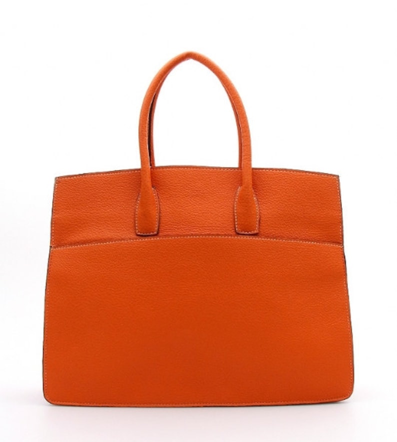 May include: A bright orange handbag with a textured surface, featuring two top handles and a structured rectangular body. The bag has visible stitching along the edges and a clean, minimalist design with a flat base and a wide opening at the top.