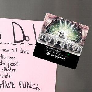 May include: A magnet with a stage scene illustration of two dancers and a crowd, with the text "Dancing Through Life". The magnet includes a Spotify code and is set against a pink background with a to-do list.