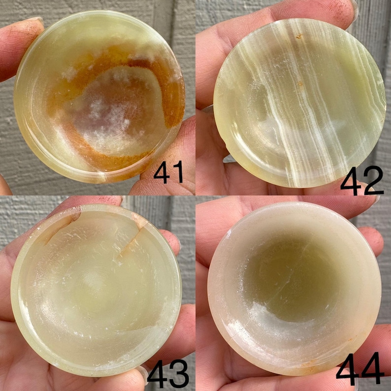 以下が含まれることがあります： 緑、黄色、茶色のさまざまな色合いの、小さくて丸い石のボウルが4つ。各ボウルはわずかに凹んだ内側を持っています。ボウルには41、42、43、44の番号が付けられています。ボウルは人の手で持たれています。