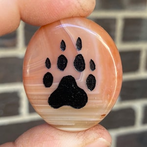 May include: A round, orange agate stone with a black paw print etched into the surface.