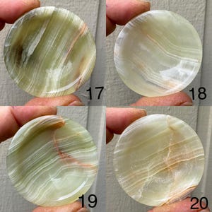以下が含まれることがあります： 緑、白、茶色の模様が施された、丸く磨かれたオニキスの石が4つ。それぞれの石には17、18、19、20の番号が振られています。石は指で持たれています。