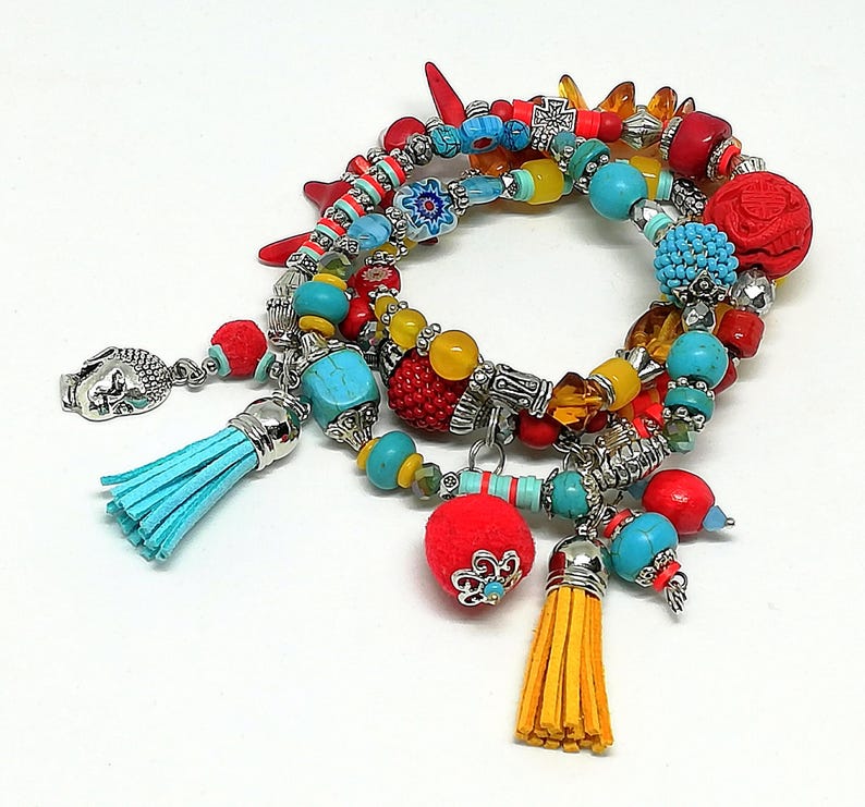 K&ouml;nnte beinhalten: Eine Sammlung farbenfroher Armb&auml;nder mit T&uuml;rkis-, Rot-, Gelb- und Silberakzenten. Die Armb&auml;nder weisen verschiedene Perlenformen auf, darunter runde, zylindrische und strukturierte Perlen, sowie Quasten- und Charm-Details.