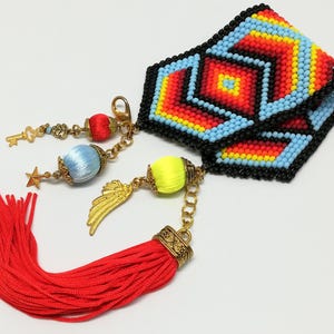 May include: A beaded cuff bracelet with a geometric pattern in red, yellow, blue, and black. The bracelet has gold-colored charms, including a key, star, and wing, and a red tassel. The bracelet is approximately 2 inches wide.