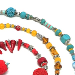 K&ouml;nnte beinhalten: Nahaufnahme von drei Perlenketten mit verschiedenen bunten Perlen. Die Halsketten weisen t&uuml;rkisfarbene, gelbe, rote und blaue Perlen sowie silberfarbene Metallakzente auf. Die Perlen sind in verschiedenen Formen und Gr&ouml;&szlig;en gehalten und schaffen ein einzigartiges und auff&auml;lliges Design.