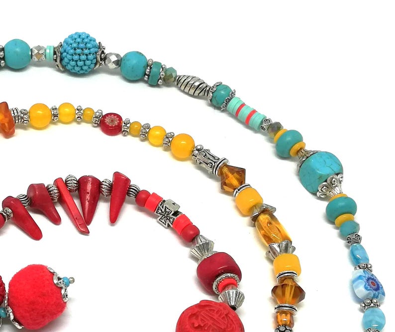 K&ouml;nnte beinhalten: Nahaufnahme von drei Perlenketten mit verschiedenen bunten Perlen. Die Halsketten weisen t&uuml;rkisfarbene, gelbe, rote und blaue Perlen sowie silberfarbene Metallakzente auf. Die Perlen sind in verschiedenen Formen und Gr&ouml;&szlig;en gehalten und schaffen ein einzigartiges und auff&auml;lliges Design.
