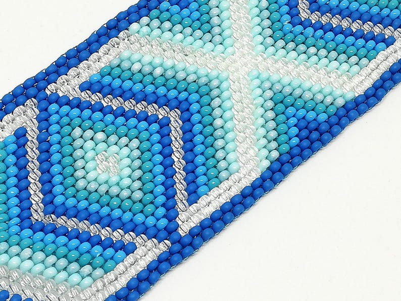 May include: Close-up of a beaded bracelet with a geometric pattern. The bracelet features a variety of blue and turquoise beads, with silver and white accents. The design is a repeating pattern of squares and diamonds.