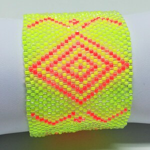 May include: A neon yellow beaded bracelet with a geometric pattern in red and orange. The bracelet is wide and appears to be made of small, square beads. The design features a central diamond shape and decorative edges.
